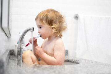 Funny,cute,caucasian naked baby girl, toddler, sitting in sink brushing teeth ,playing in bathroom,...