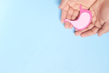 Top view of human hand holding stomach paper cutout. Stomach care, health, healthy digestion and ulcer prevention concept.