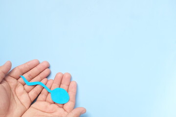 Top view of male hand holding sperm cutout in blue background. Men's health, sperm donation and...