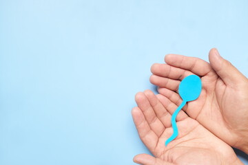 Top view of male hand holding sperm cutout in blue background. Men's health, sperm donation and...