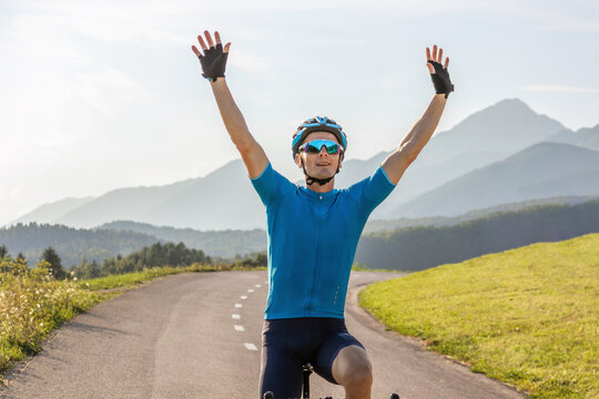 Male athlete professional racing cyclist riding a bike with arms raised above the head, in a victory pose