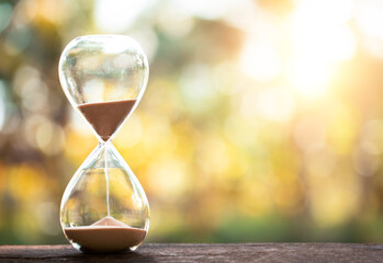 hourglass (sand clock) on an old wooden table with natural blur background, Hourglass as time passing concept for business deadline, Life-time passing concept, elapsed time concept, copy space