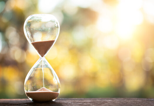 hourglass (sand clock) on an old wooden table with natural blur background, Hourglass as time passing concept for business deadline, Life-time passing concept, elapsed time concept, copy space