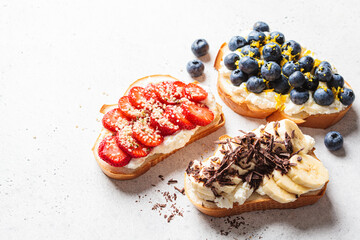 Fruity vegetarian toasts for breakfast on gray background. Bread slices with ricotta, berries, banana, chocolate and seeds.
