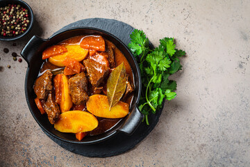 Beef stew with potatoes, carrots in tomato sauce in black pot,  dark background.