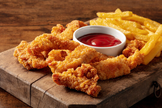 Chicken tenders, battered and fried crispy wedges, with a bbq sauce and potato, on a dark rustic wooden table