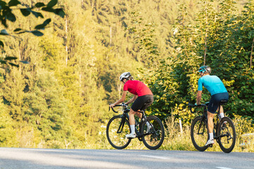 Naklejka premium Two professional cyclist racers, male and female during training on a paved road through the mountain landscape, front view.