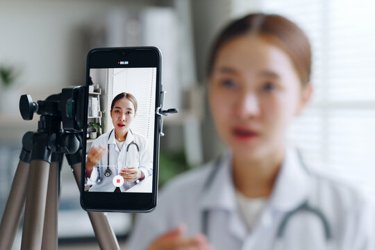 Asian woman doctor making online live streaming broadcast talking over camera recording in hospital, medical and healthcare blogger, vlogger concept