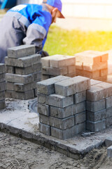 Bricklayer in work clothes sits on sidewalk and lays out paving slabs. Sight of working man in open air. Professional builder makes arrangement of territory summer day. Real scene.