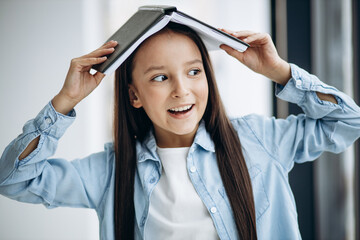 Little school girl with book at home