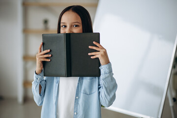 Little school girl with book at home