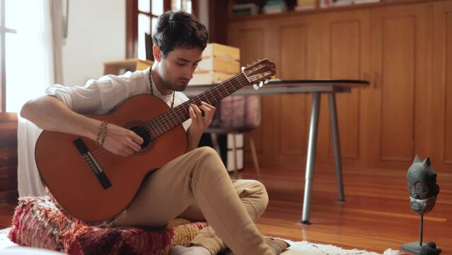 Young adult plays guitar in his bedroom in a relaxed, almost meditative way letting energy flow