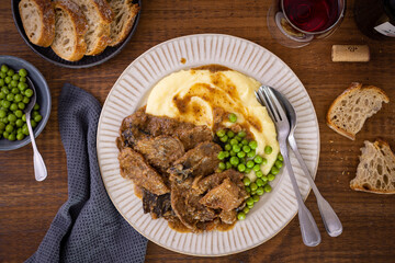 Fricando, typical dish of Catalan cuisine of stewed beef, served with mashed potatoes and peas on a dark wooden table. By his side bread and a glass of wine.