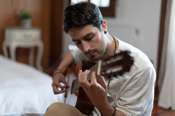Obraz premium Young adult plays guitar in his bedroom in a relaxed, almost meditative way letting energy flow