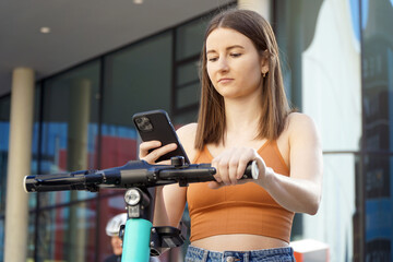 Fototapeta na wymiar Young woman rents an e-scooter via a smartphone app