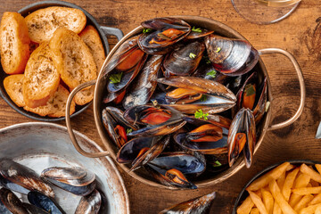 Belgian mussels with French fries and toasted bread, overhead flat lay shot on a rustic wooden background