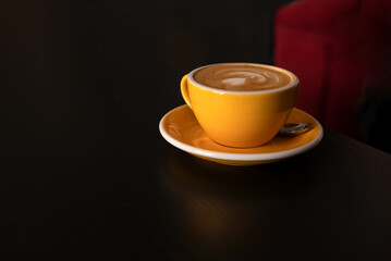 yellow coffee cup filled with cappuccinno with frothy milk foam on table.  Drinking morning coffee