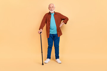 Photo of pretty funny guy pensioner dressed brown shirt glasses holding walking cane isolated beige color background