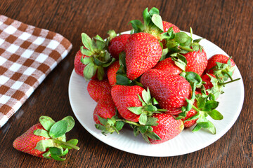 heap of garden strawberries on white plate on wooden background, close-up