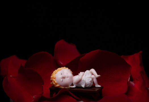 image of rose petals miniature angel figure dark background 