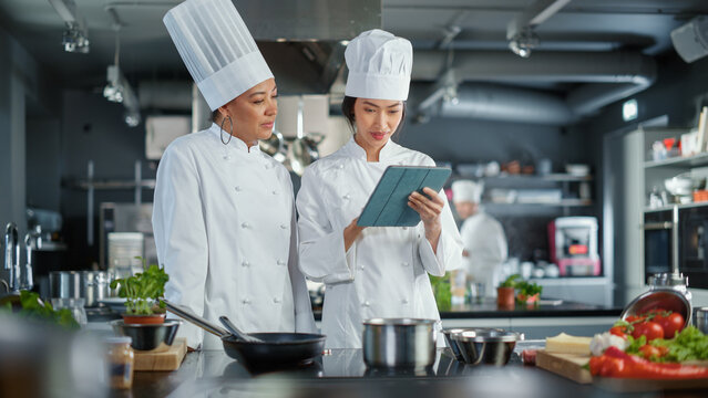 Restaurant Kitchen: Team of Asian and Black Female Chefs use Tablet Computer while Cooking Delicious and Authentic Food. Perfect Teamwork in Preparing Healthy Meal, Fusion Cuisine Dish