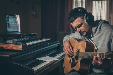 Male musician plays the guitar at home in the workplace near the computer.