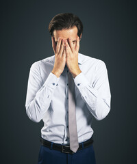 Stress and find solution concept with man in white shirt closing his eyes, facepalm isolated on dark grey background