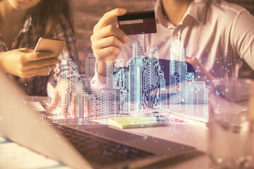 Double exposure of man and woman on-line shopping holding a credit card and town hologram drawing. Smart city concept.