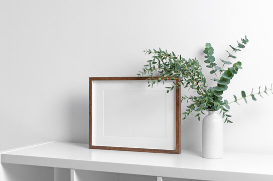 Wooden frame mockup in white room interior with fresh eucalyptus plant in vase