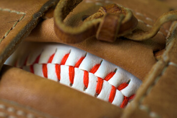 White Baseball with Red Stitching.  Baseball shows through the rawhide webbing of a baseball glove.