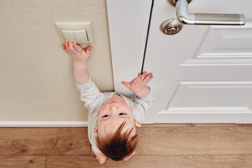 Toddler baby boy reaches for the light switch. Child turns on the light in the home
