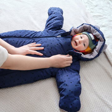 A mother woman puts on a warm jacket for a baby boy. Mom dresses a happy child in winter clothes on the bed.
