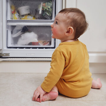 Toddler Baby Boy With Allergies On Red Cheeks Climbed Into An Open Refrigerator. Child Safety Issues In The Home Room, Little Kid