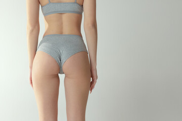 Cropped image of slim fit female body, buttocks in underwear isolated over grey studio background....