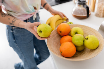 cropped view of woman in jeans near bowl with fresh fruits and blurred coffee pot in kitchen