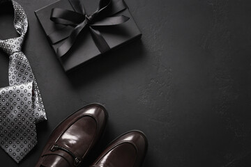 Happy Fathers Day greeting card with gift box. Set of classic mens clothes - brown shoes, tie and gift on black background. Men's accessories set. Top view. Copy space. - Powered by Adobe