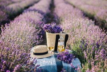 Two glasses with white wine and bottle on background of a lavender field. Straw hat and basket with...