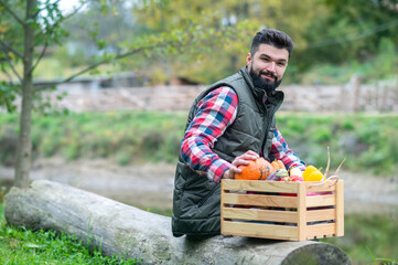 A dark-haired man in plaid shirt with a box with veggies