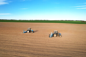 Tractor sowing seed on plowed field. Sowing seeds of corn and sunflower. Blue Tractor with disk harrow on plowing field. Seeding machinery on farm field. Seed sowing in farmland, aerial view..