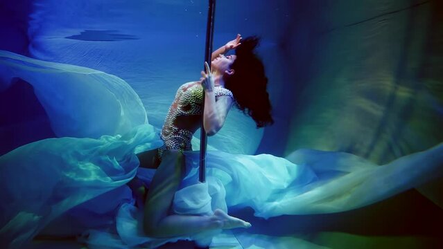 Slow motion adorable slender woman in a pearl dress dancing on a pole underwater