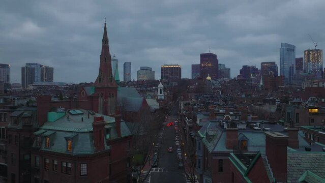 Aerial descending footage of residential urban neighbourhood at twilight. Modern high rise office buildings in background. Boston, USA