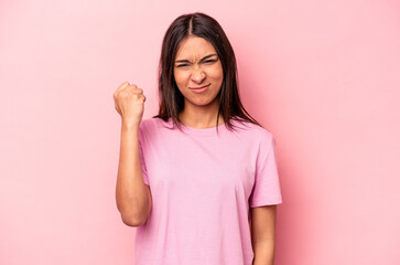 Young hispanic woman isolated on pink background showing fist to camera, aggressive facial expression.