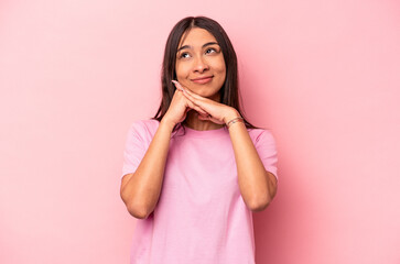 Young hispanic woman isolated on pink background keeps hands under chin, is looking happily aside.