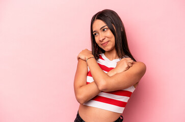 Young hispanic woman isolated on pink background hugs, smiling carefree and happy.