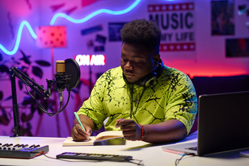 Portrait of creative young gen Z African American man sitting at desk in home studio working on...