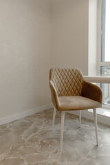 A free-standing chair with soft upholstery in a rhombus of beige color against the background of a monochromatic part of the interior, a beige wall