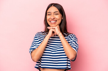 Young hispanic woman isolated on pink background keeps hands under chin, is looking happily aside.