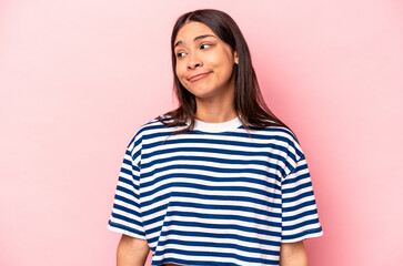 Young hispanic woman isolated on pink background shrugs shoulders and open eyes confused.
