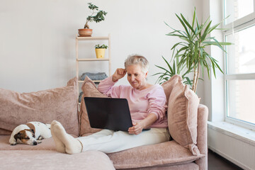 Older smiling 60s woman sitting at home on sofa