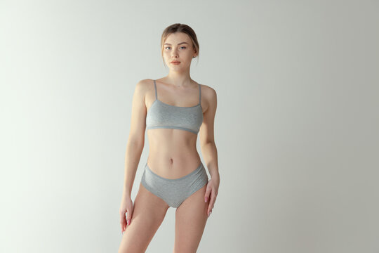 Portrait of yound tender girl with toned fit body posing in underwear isolated over grey studio background